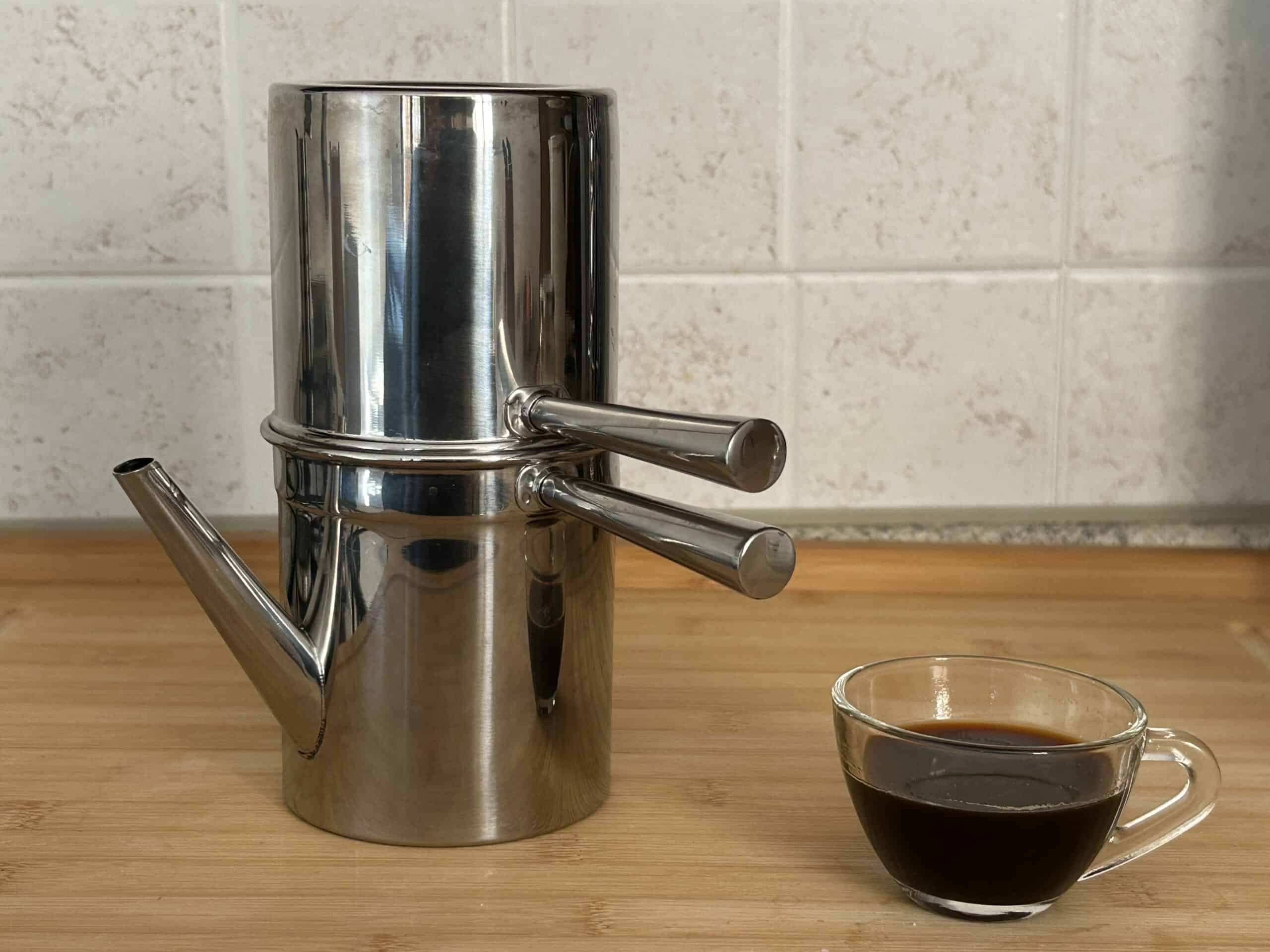 Cuccumella napoletana in acciaio con una tazzina di caffè su un piano in legno.