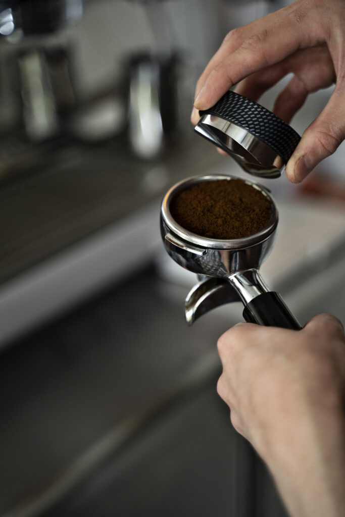 Barista che usa un distributore di caffè nel portafiltro per livellare il macinato prima del tamping.