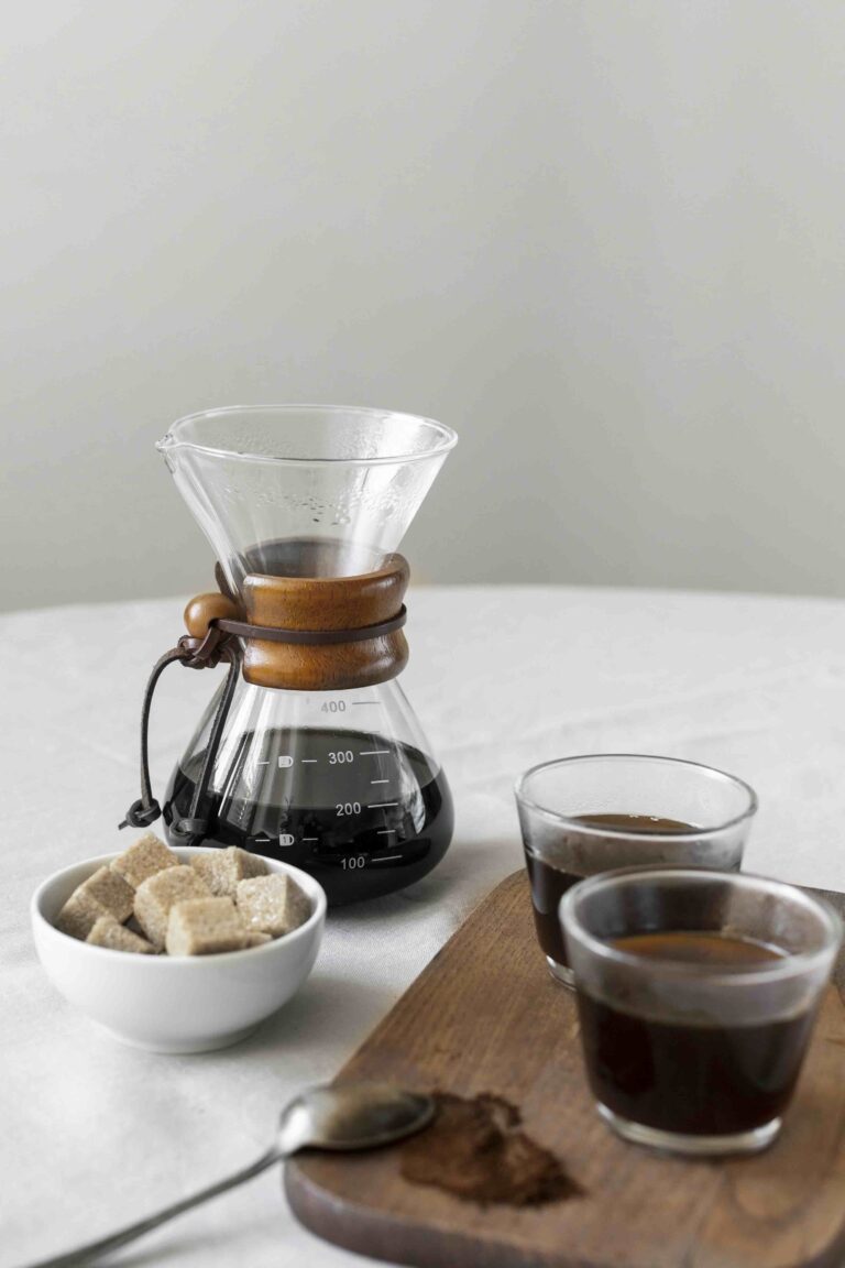 Chemex con caffè filtrato appena preparato accanto a due tazze e zucchero di canna su un tavolo