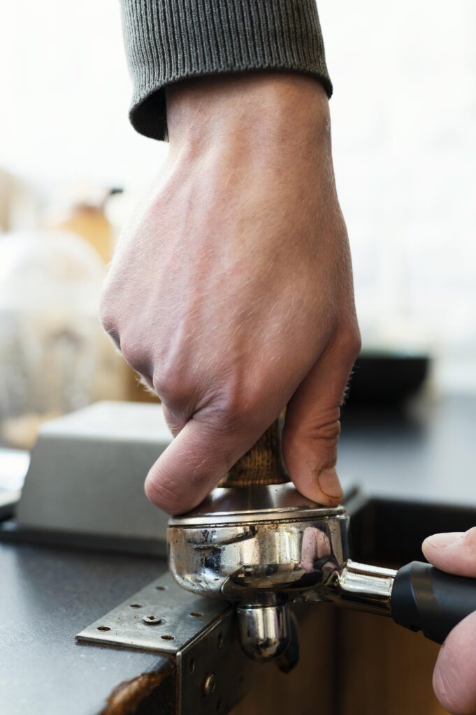Barista che pressa il caffè nel portafiltro con un tamper.
