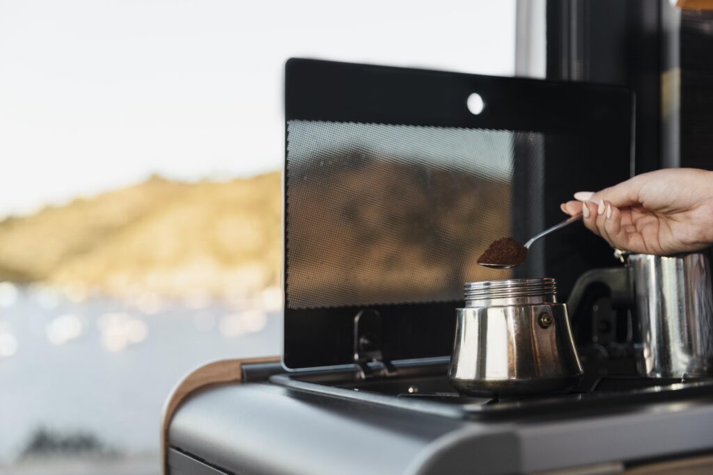 Mano che versa caffè macinato nella caldaia della moka con un cucchiaino