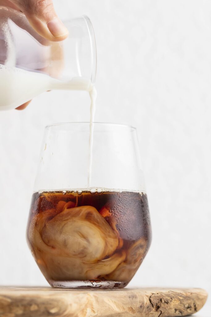 Latte versato in bicchiere di cold brew con ghiaccio e vortici cremosi