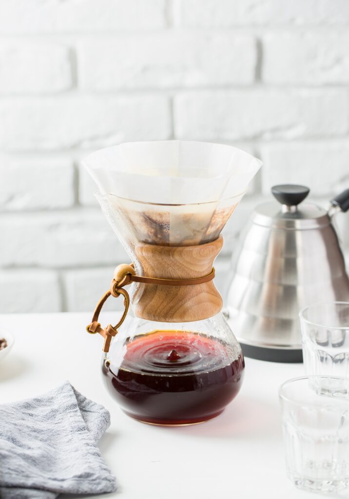 Chemex con caffè filtrato e kettle in acciaio su tavolo chiaro