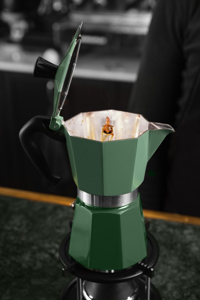 Caffè che sale dalla colonnina di una moka verde con il coperchio aperto durante l’estrazione
