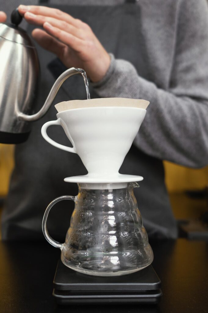 Acqua versata in filtro V60 con kettle a becco stretto su caraffa in vetro