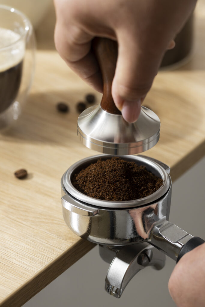 Mano che usa un tamper per pressare il caffè macinato nel portafiltro, primo piano della tecnica di tamping.